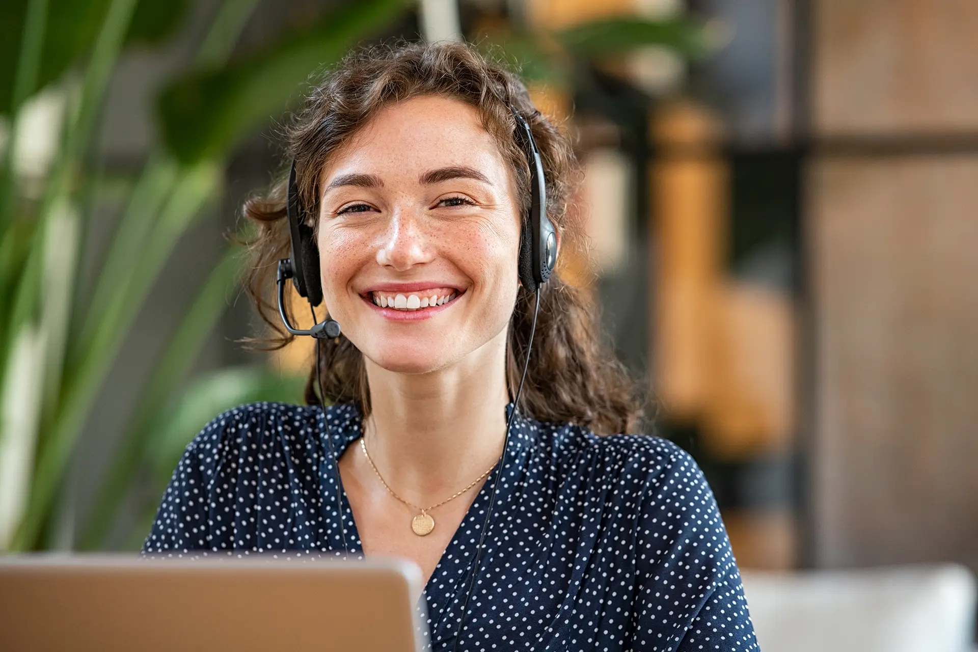 Smiling woman wearing a headset, seated at a laptop.