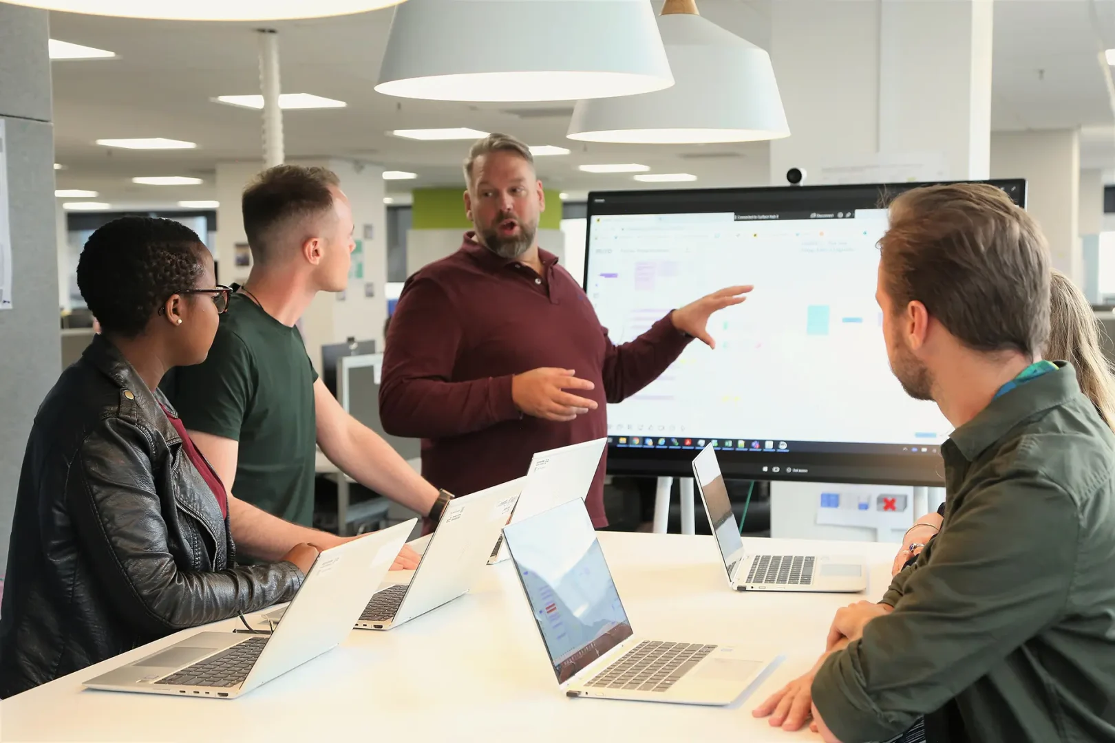 Several people sit around a large table in a modern office, looking toward a screen displaying a presentation. Laptops are open, and the setting suggests a focused team meeting or training session in a collaborative work environment at EPL