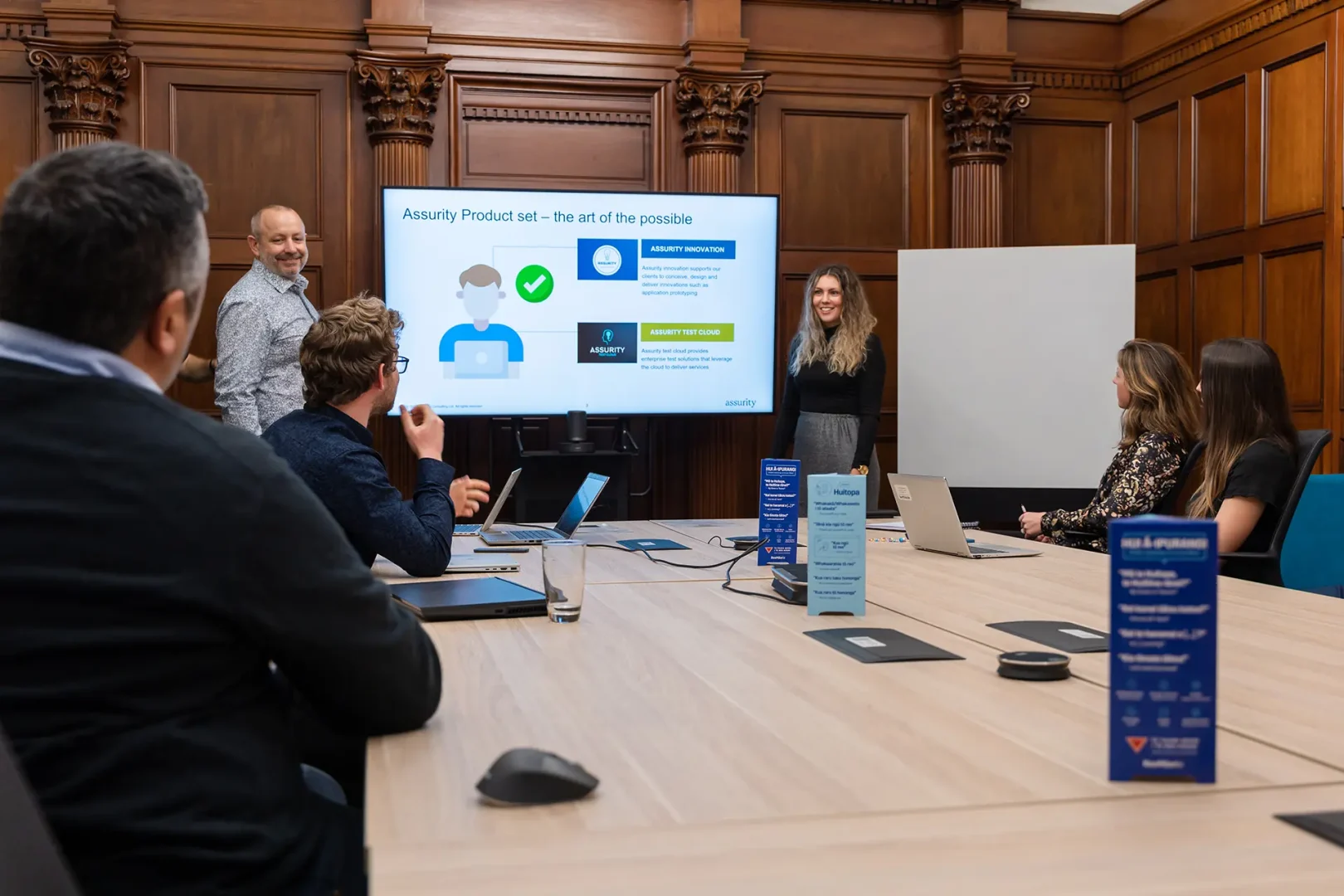 People in a conference room watching a presentation titled “Assurity Product set – the art of the possible.