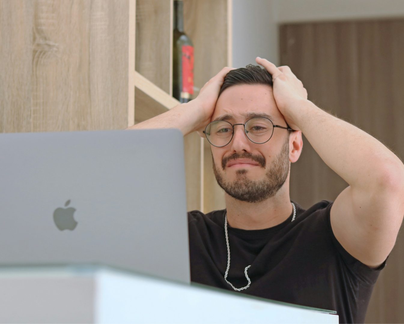Person sitting in front of a laptop with hands on head, appearing focused or deep in thought.