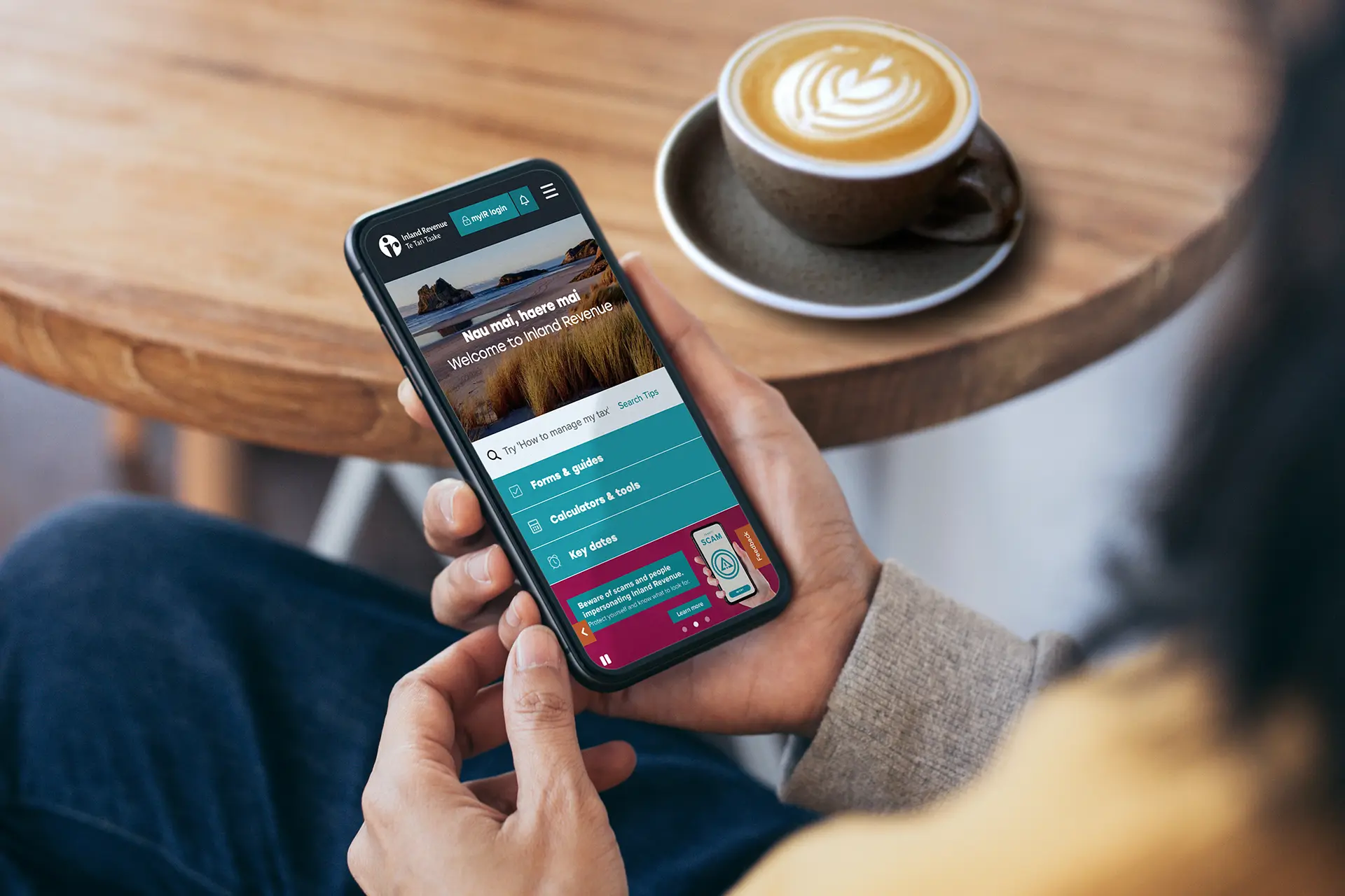 Woman using the Inland Revenue website on her phone while having coffee at a café.