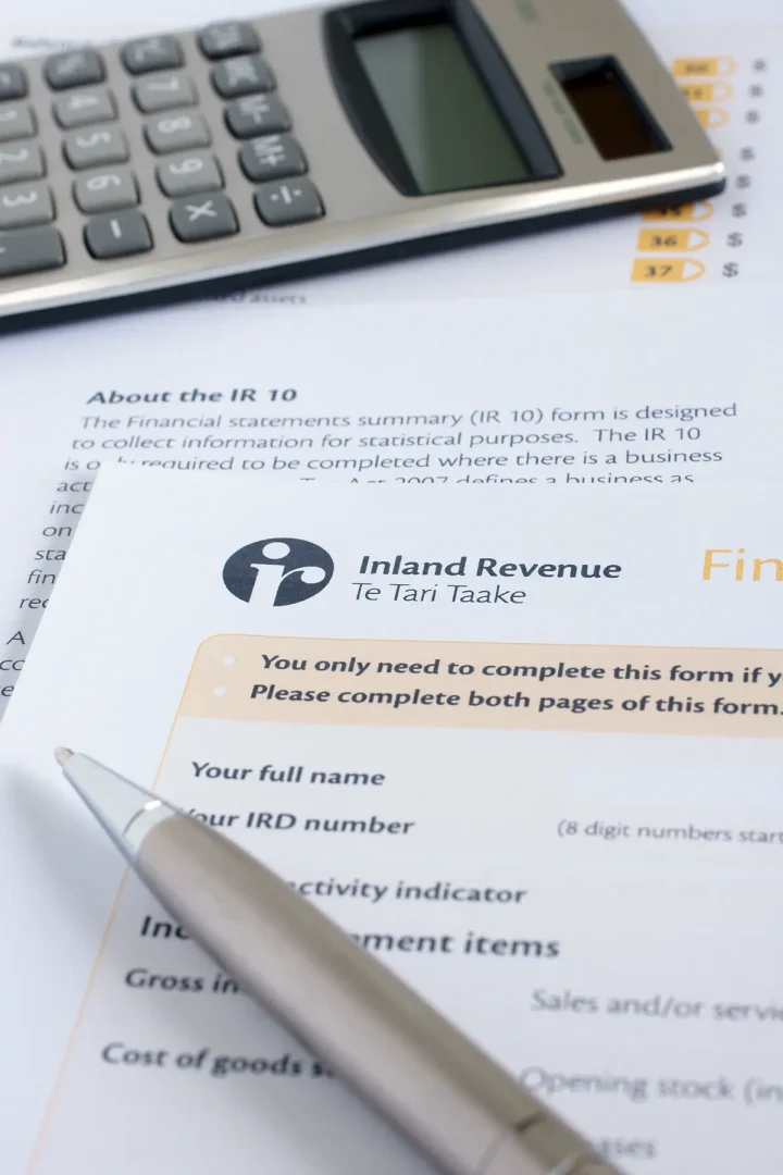 A pen rests on a partially filled Inland Revenue form with a calculator in the background. The form includes fields for name, IRD number, and financial details.