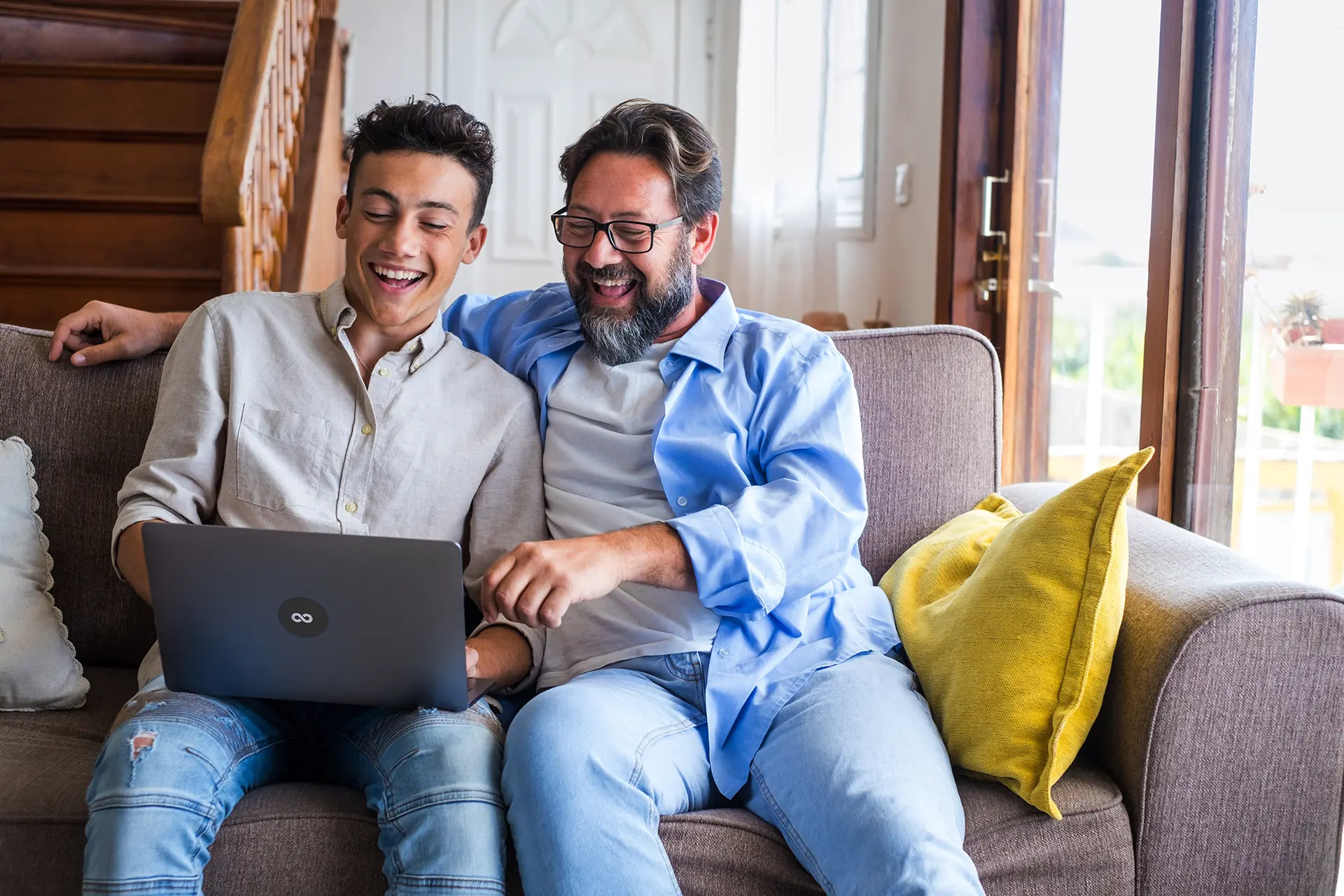Teenager and adult celebrating exam results while looking at a laptop on a couch at home.