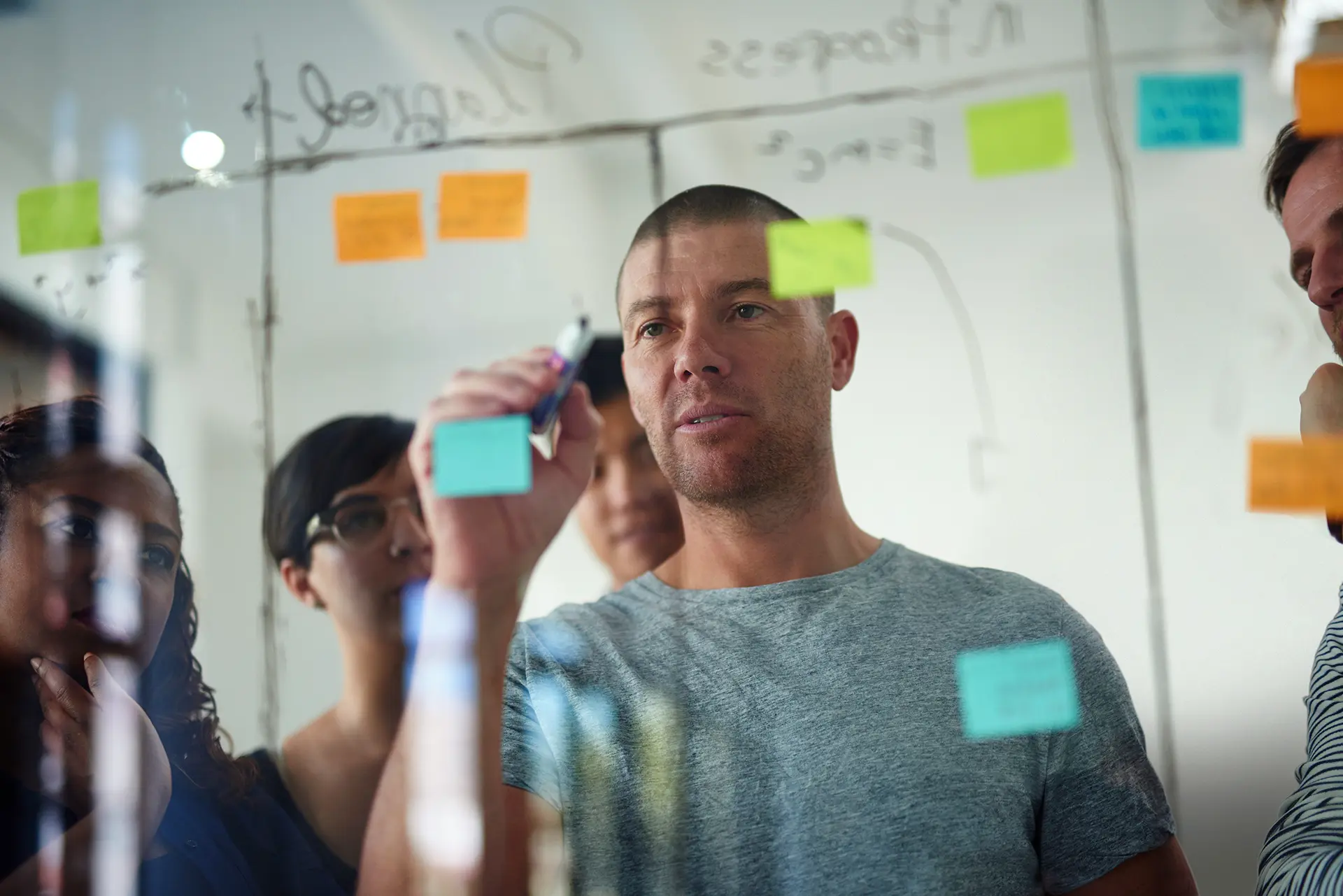 Group of people collaborating in an office, writing on a glass board covered with colorful sticky notes.