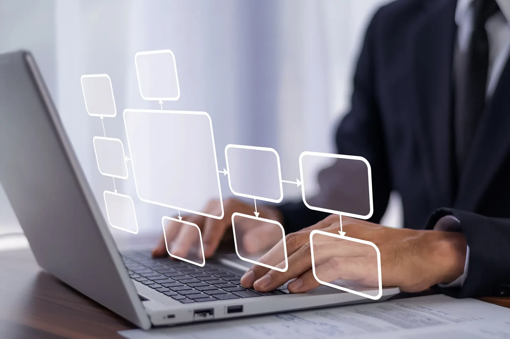 Person in a suit typing on a laptop with a floating flowchart diagram overlayed above the keyboard.