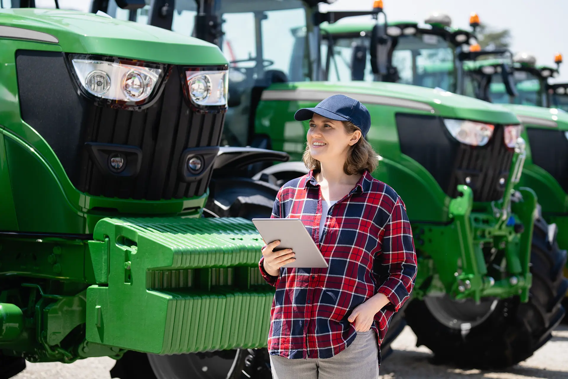 Woman holding a tablet while inspecting green tractors, at a a leading farm equipment supplier.