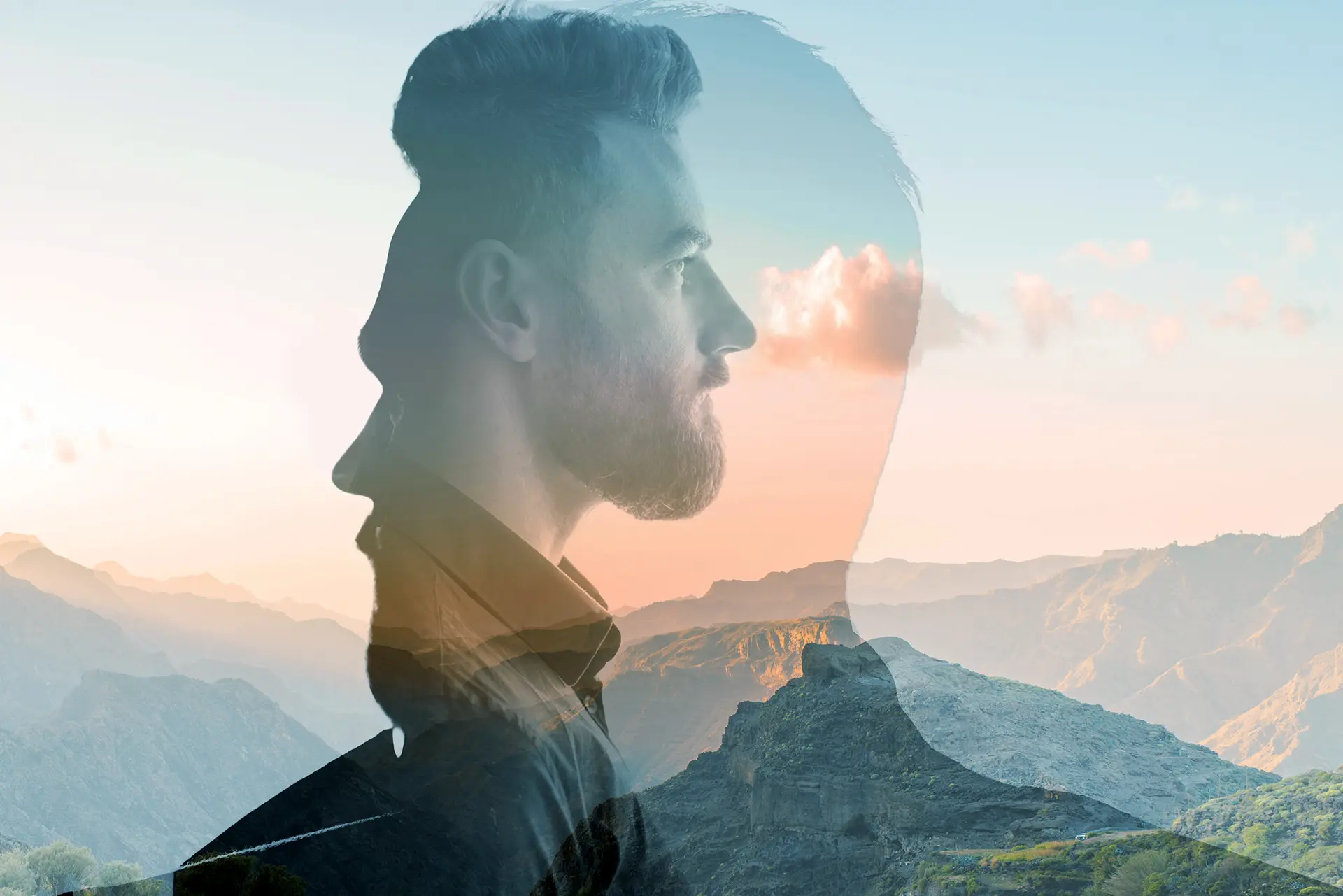 A bearded man looks out over a majestic mountain range in a striking double exposure image.