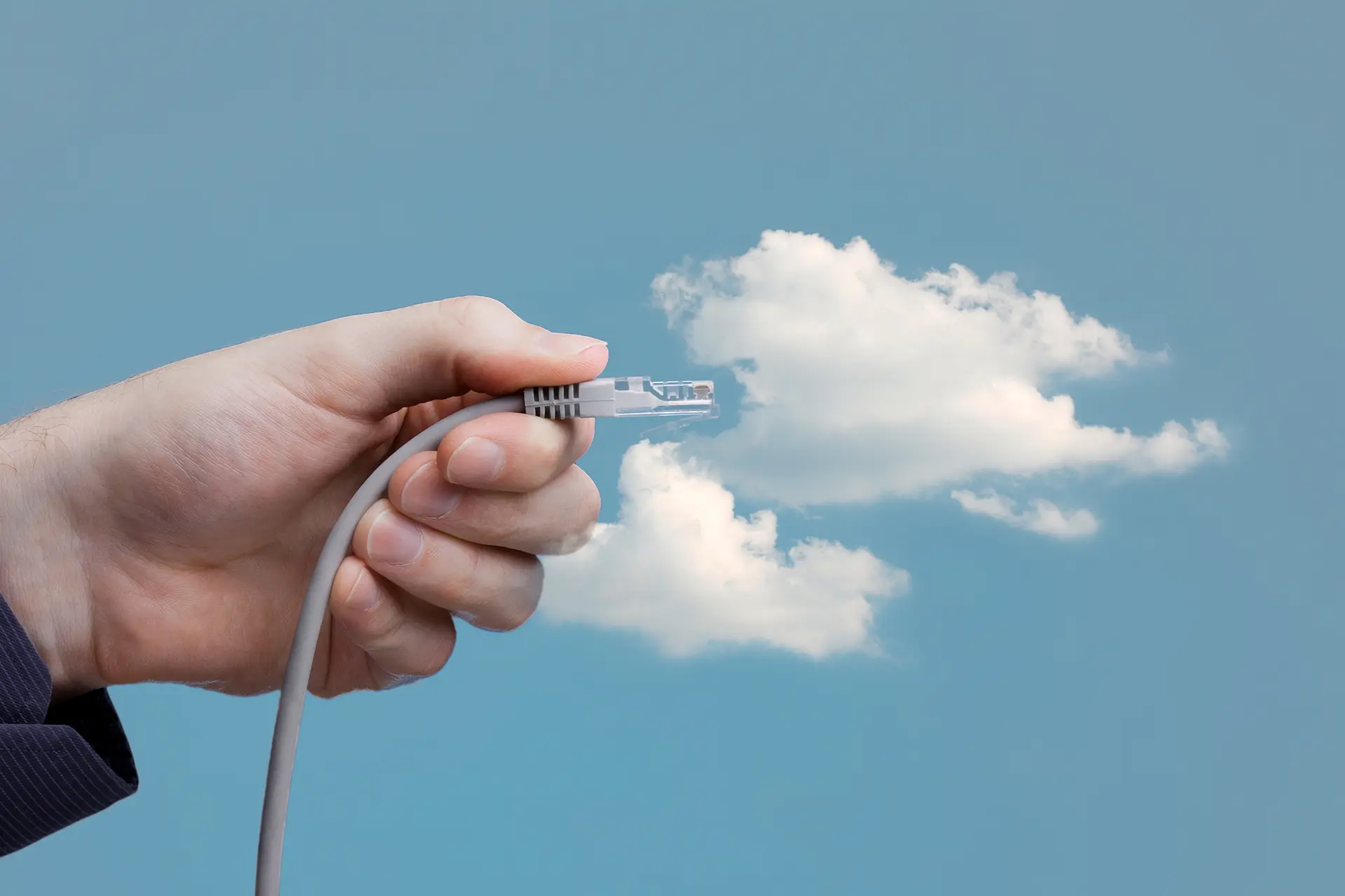 Hand holding an Ethernet cable toward clouds, symbolizing cloud computing.